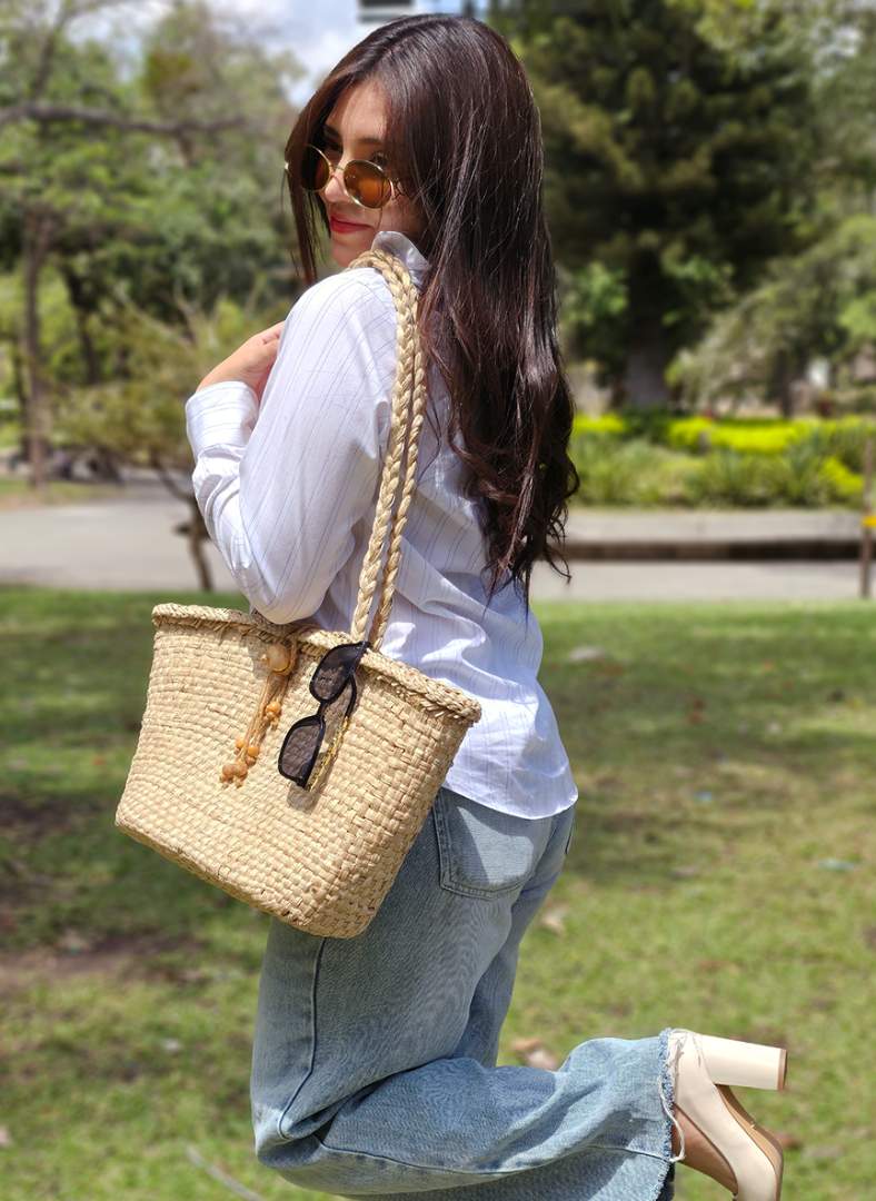 Modelo mujer hermosa luciendo un bolso de verano hecho a mano por artesanos salvadorenos con materiales naturales